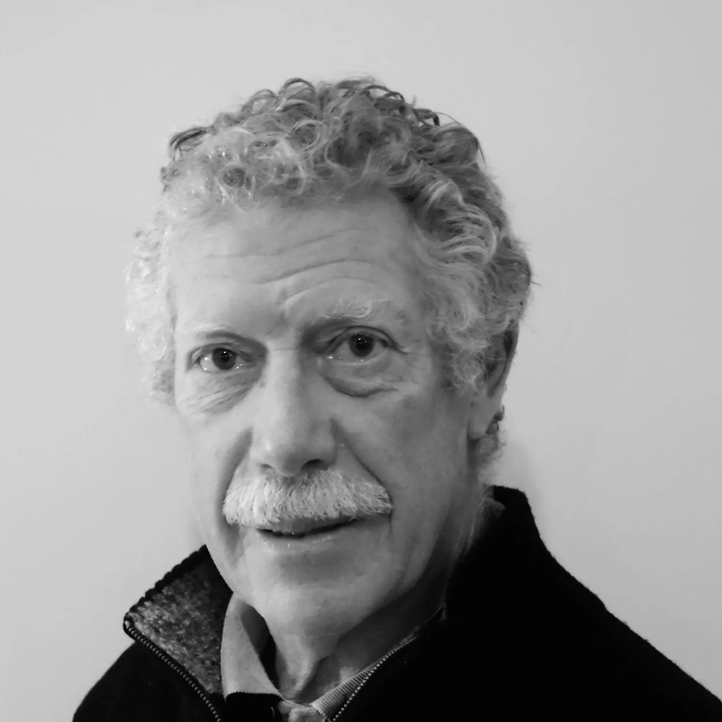 A black and white photo of a person with curly hair, glasses, and a beard, looking directly at the camera.