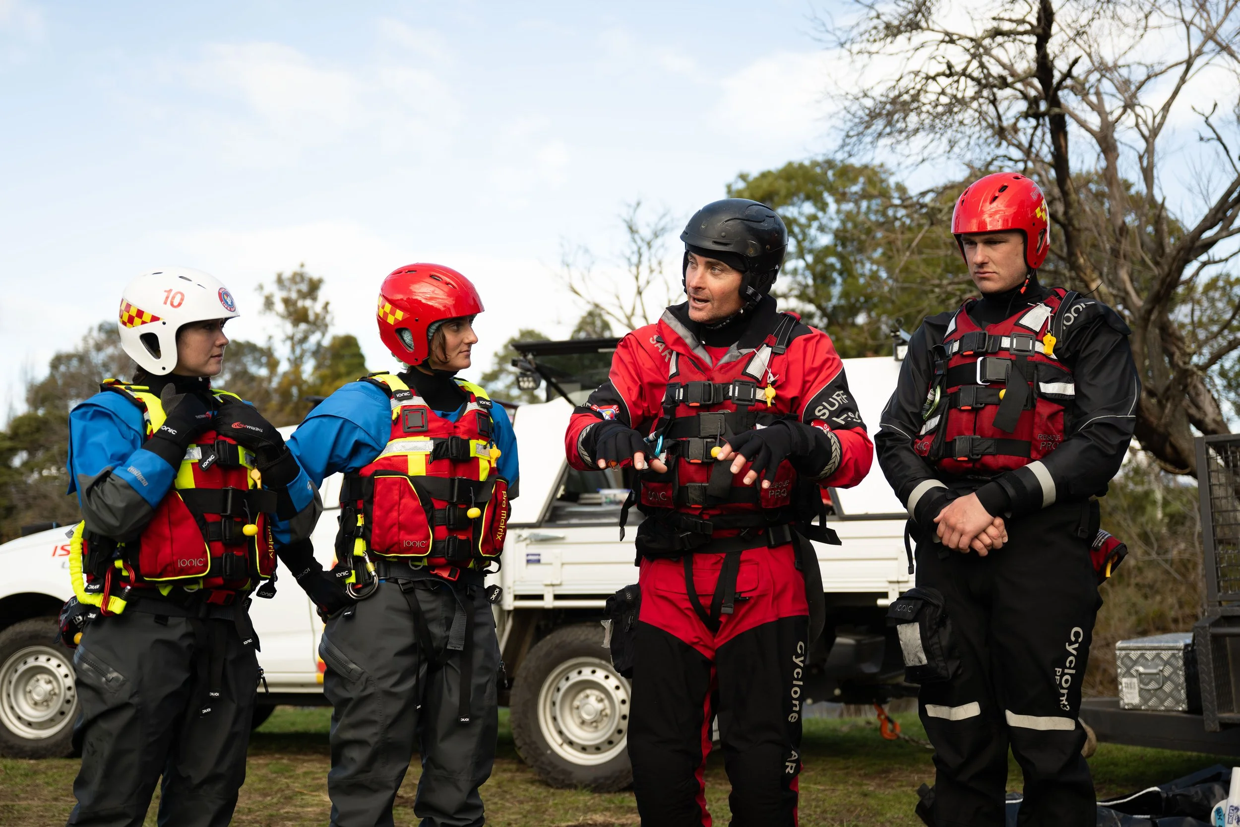 Four rescue workers wearing helmets and safety vests standing outdoors and having a conversation.