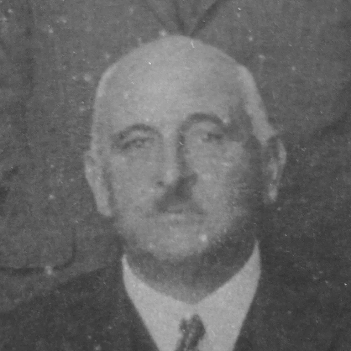 A black and white portrait of a man with glasses, short hair, wearing a collared shirt and tie.