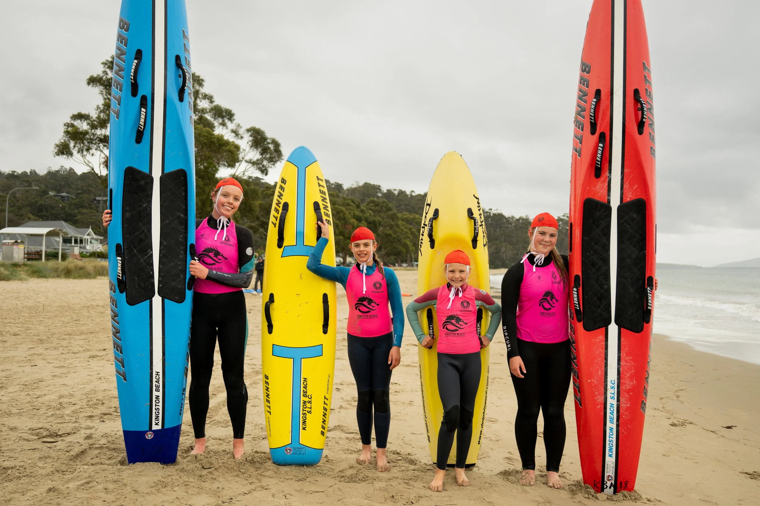 A surfboard rider wearing a red an yellow cap and yellow swimsuit riding a wave on a yellow surfboard under a partly cloudy sky.
