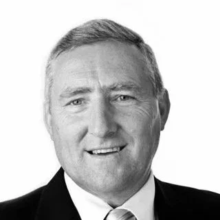 Black and white headshot of a smiling middle-aged man in a suit and tie.