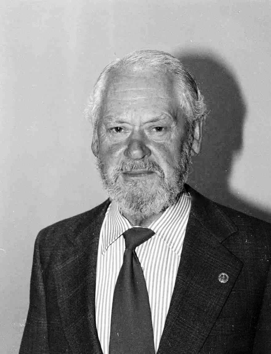 Black and white photo of an elderly man with white hair and beard, wearing a suit and tie, looking at the camera.