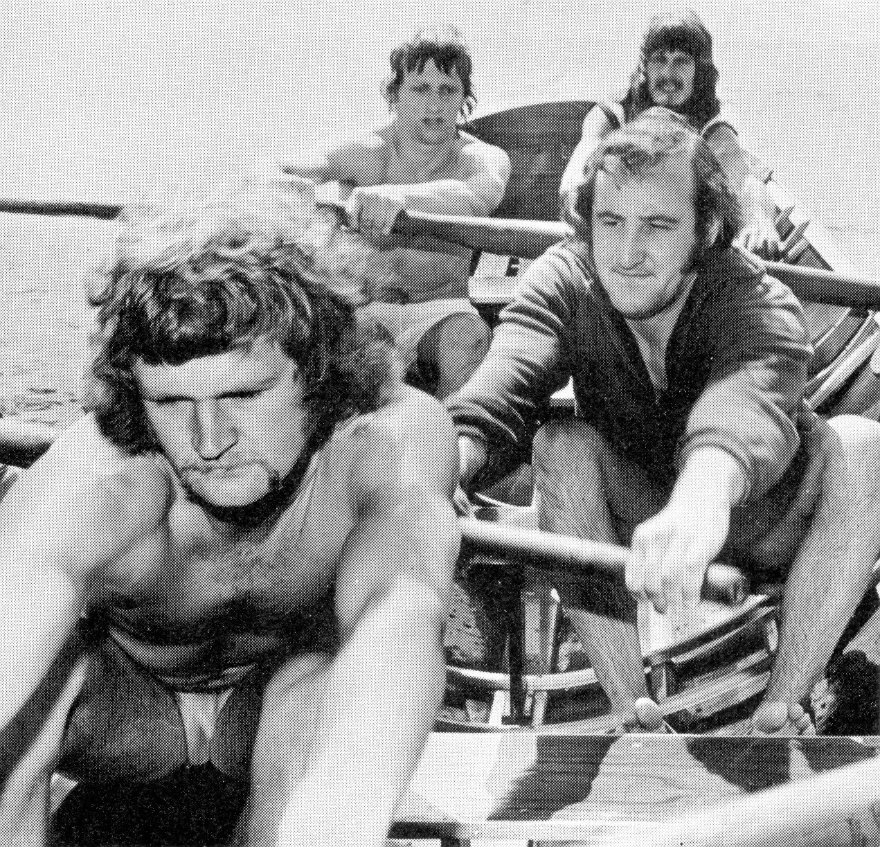 Four young men riding go-karts on a race track, with one in the foreground steering and the others behind him, all in casual clothing.