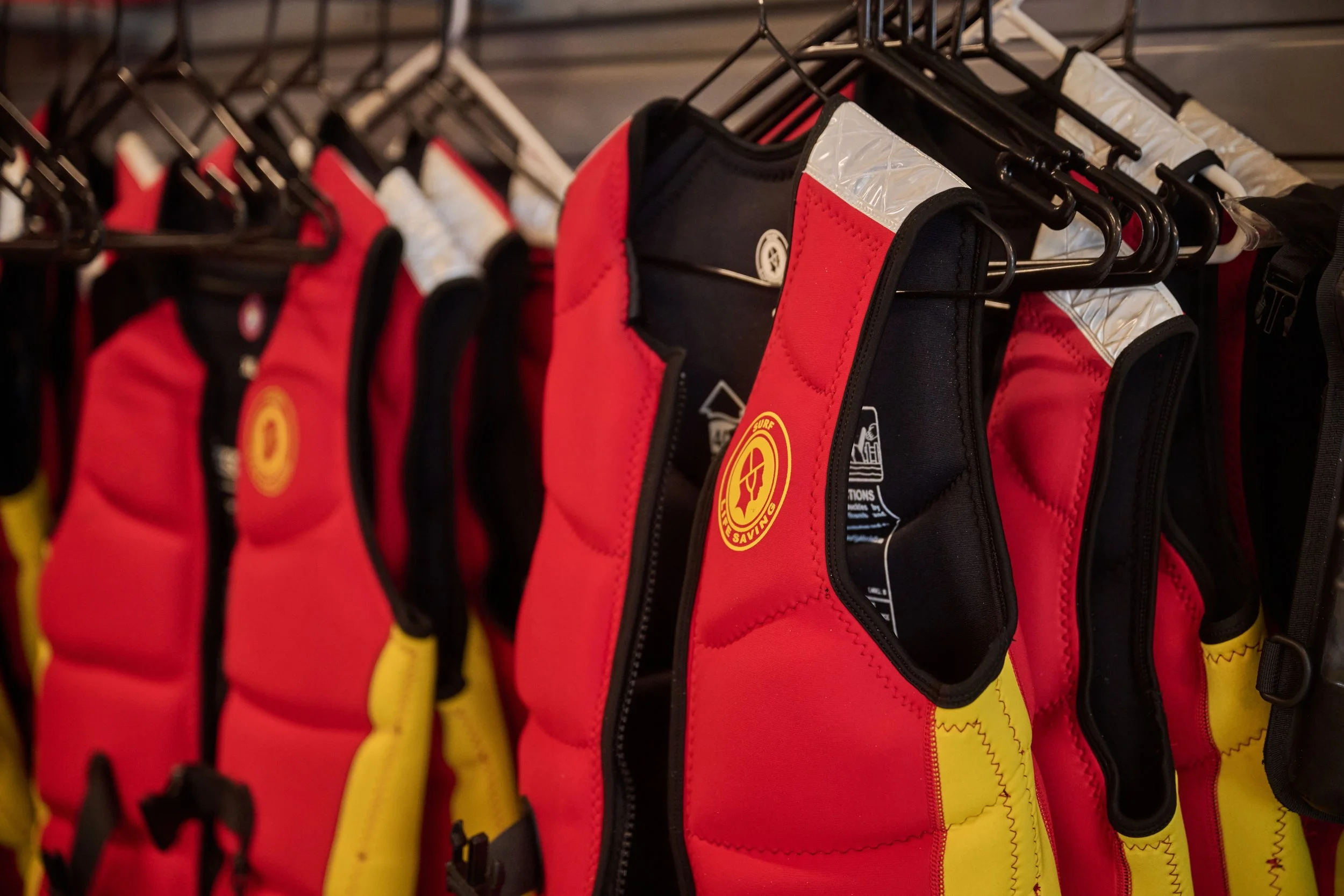 Life jackets hanging on a rack in red, black, and yellow colors.