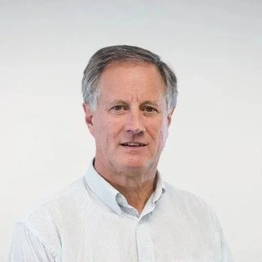 A middle-aged man with short gray hair wearing a white dress shirt standing against a plain white background.