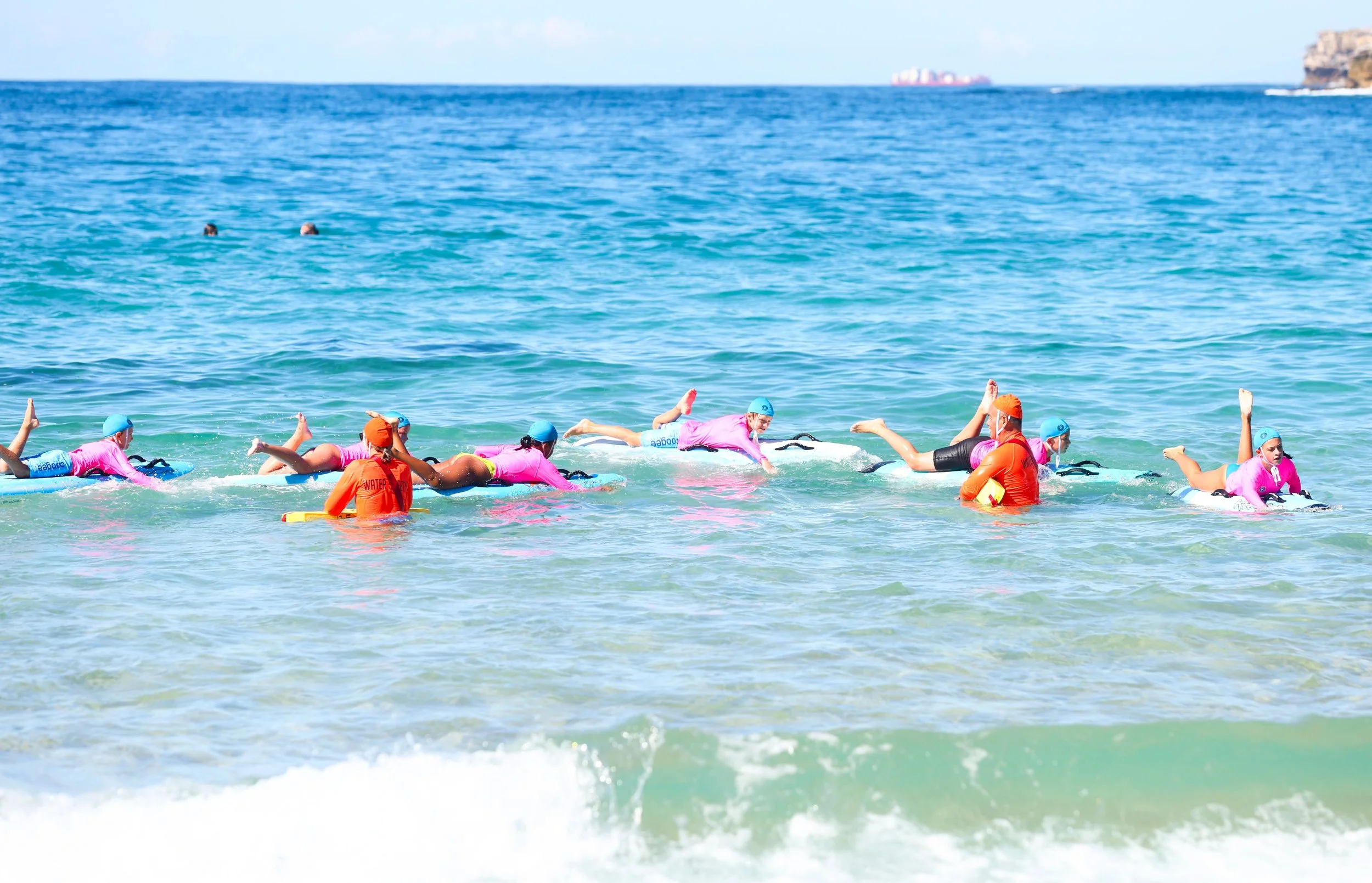 People swimming in the ocean with some wearing wetsuits and swim caps.