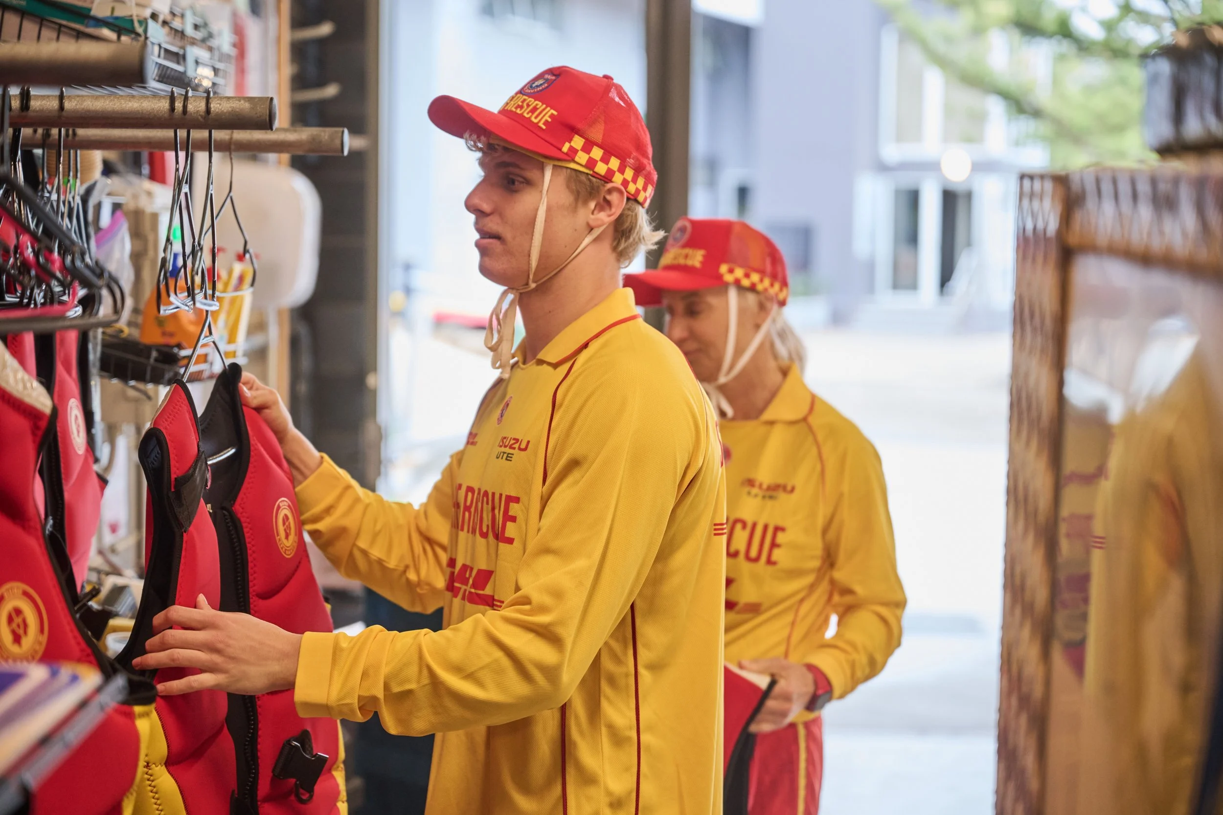 Two individuals wearing yellow jackets and red fire rescue hats browsing equipment in a storage area.