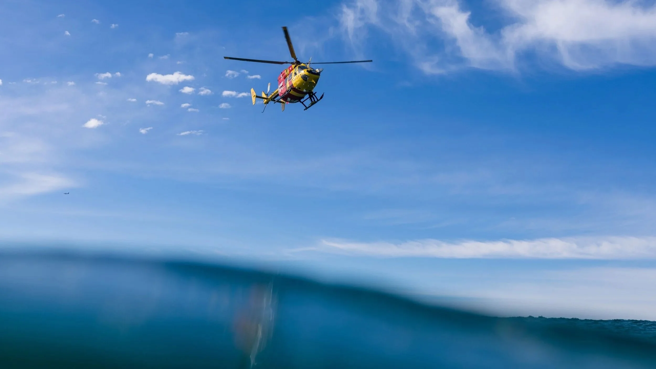 A helicopter flying in a clear blue sky with some clouds.
