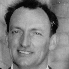Black and white photo of a man with short dark hair, smiling at the camera.