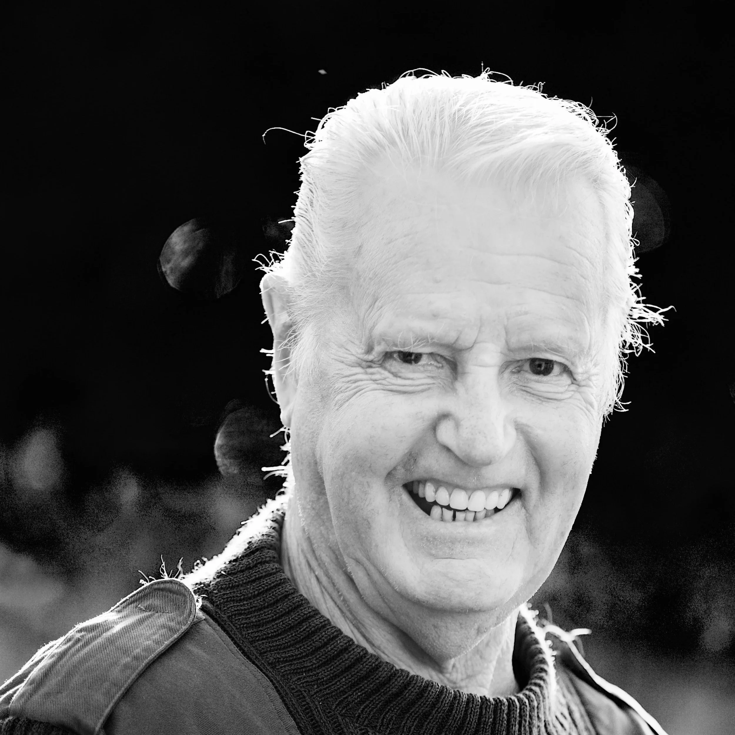 Black and white photo of a joyful man with short hair, smiling with visible teeth, wearing a jacket.