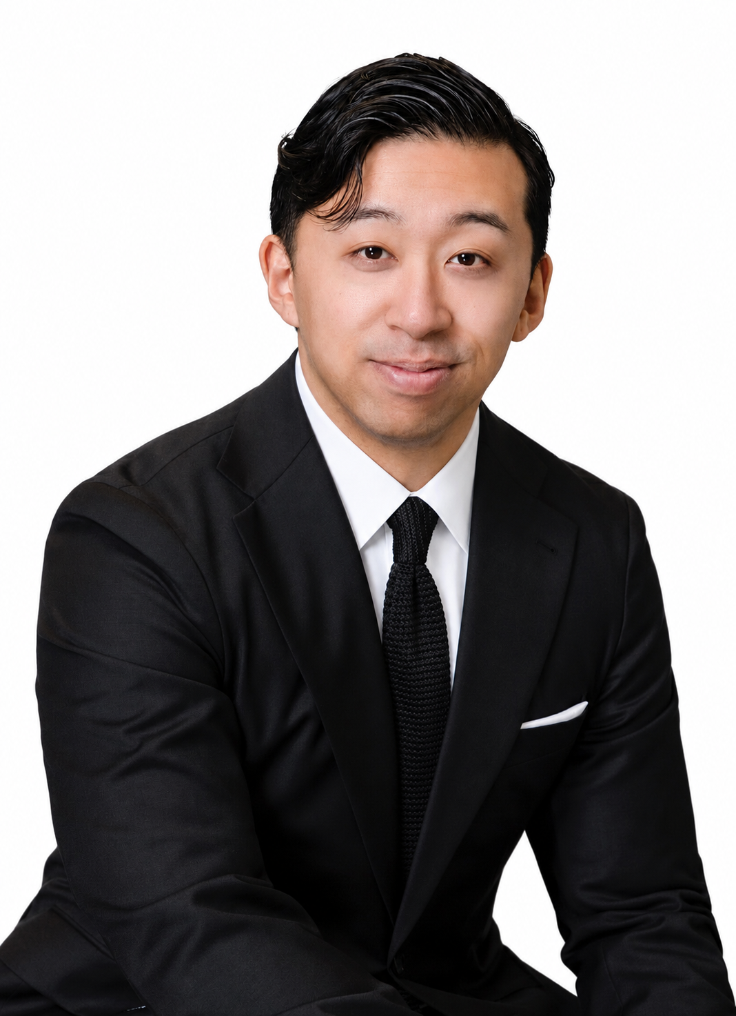 Professional portrait of an Asian man in a black suit and tie, sitting against a white background.