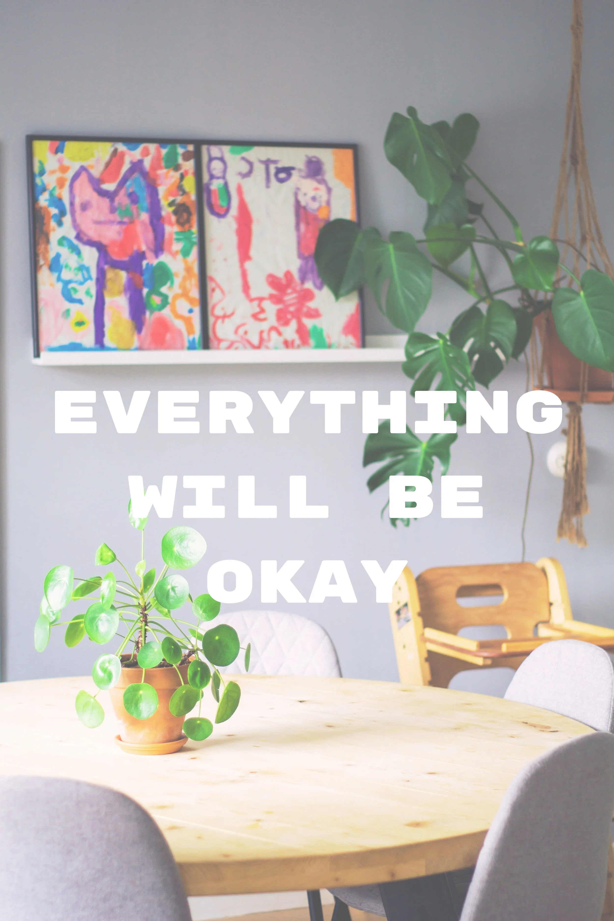 A round wooden table with a potted green plant in a terracotta pot. In the background, there is wall decor with colorful artwork and a green leafy plant next to a macramé plant hanger. The ceiling and wall are gray, and there are wooden chairs around the table. Overlaid white text reads 'EVERYTHING WILL BE OKAY'.