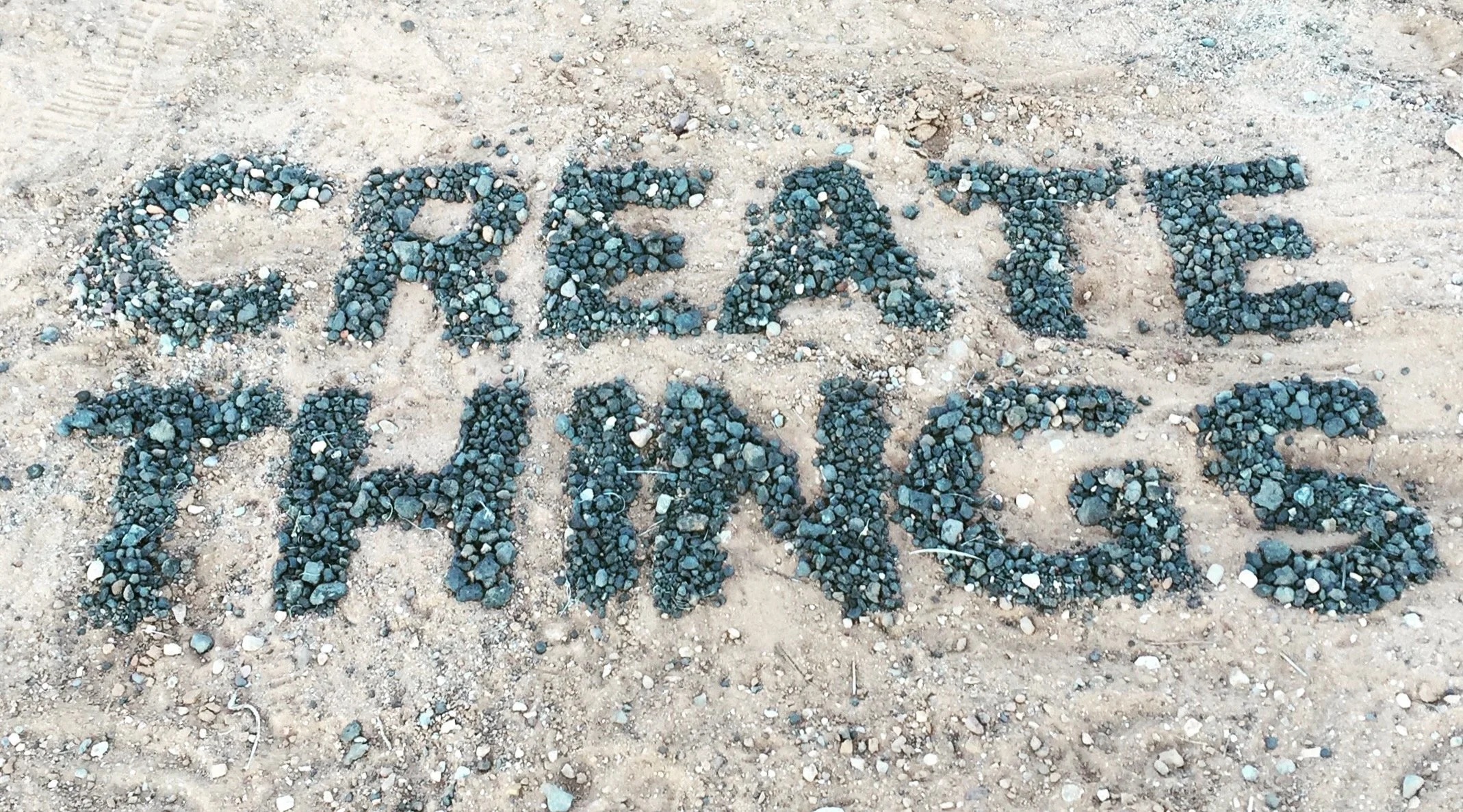 Sand with the words 'CREATE MORE' written using small dark stones.