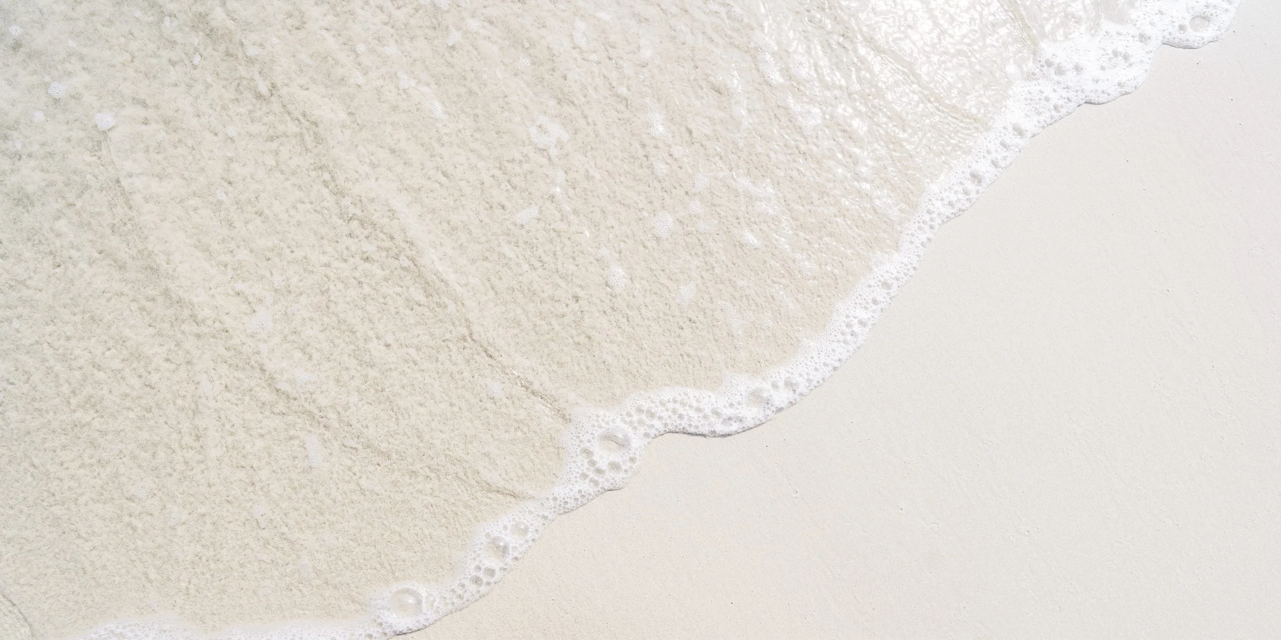 Close-up of gentle waves washing onto a sandy beach.