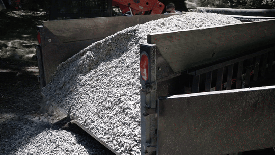 A dump truck filled with white gravel or small stones, with some spilling over the side.