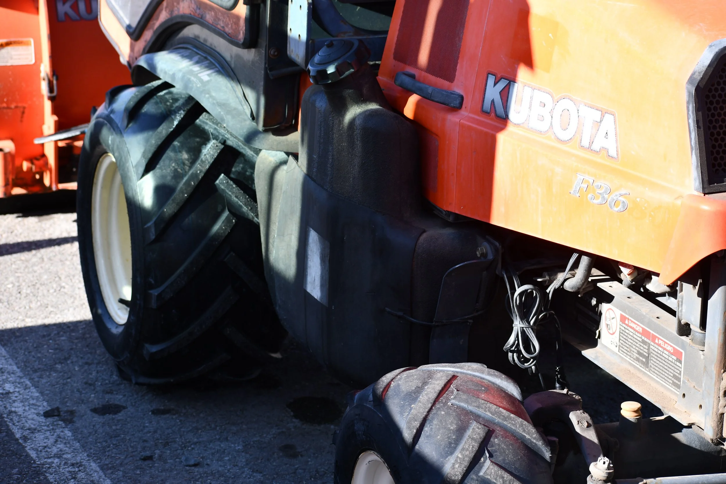 Close-up of a Kubota F36 compact tractor with front loader attachment and large black tires, parked outdoors on a gravel surface.