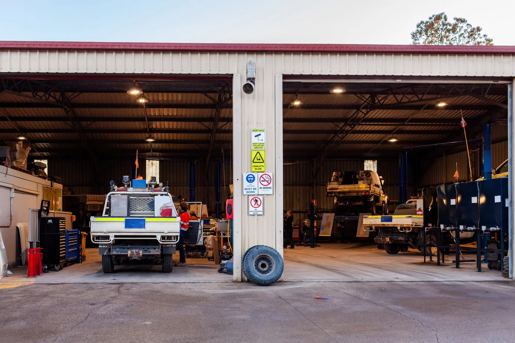 Open vehicle service garage with various tools, vehicles, and workers.