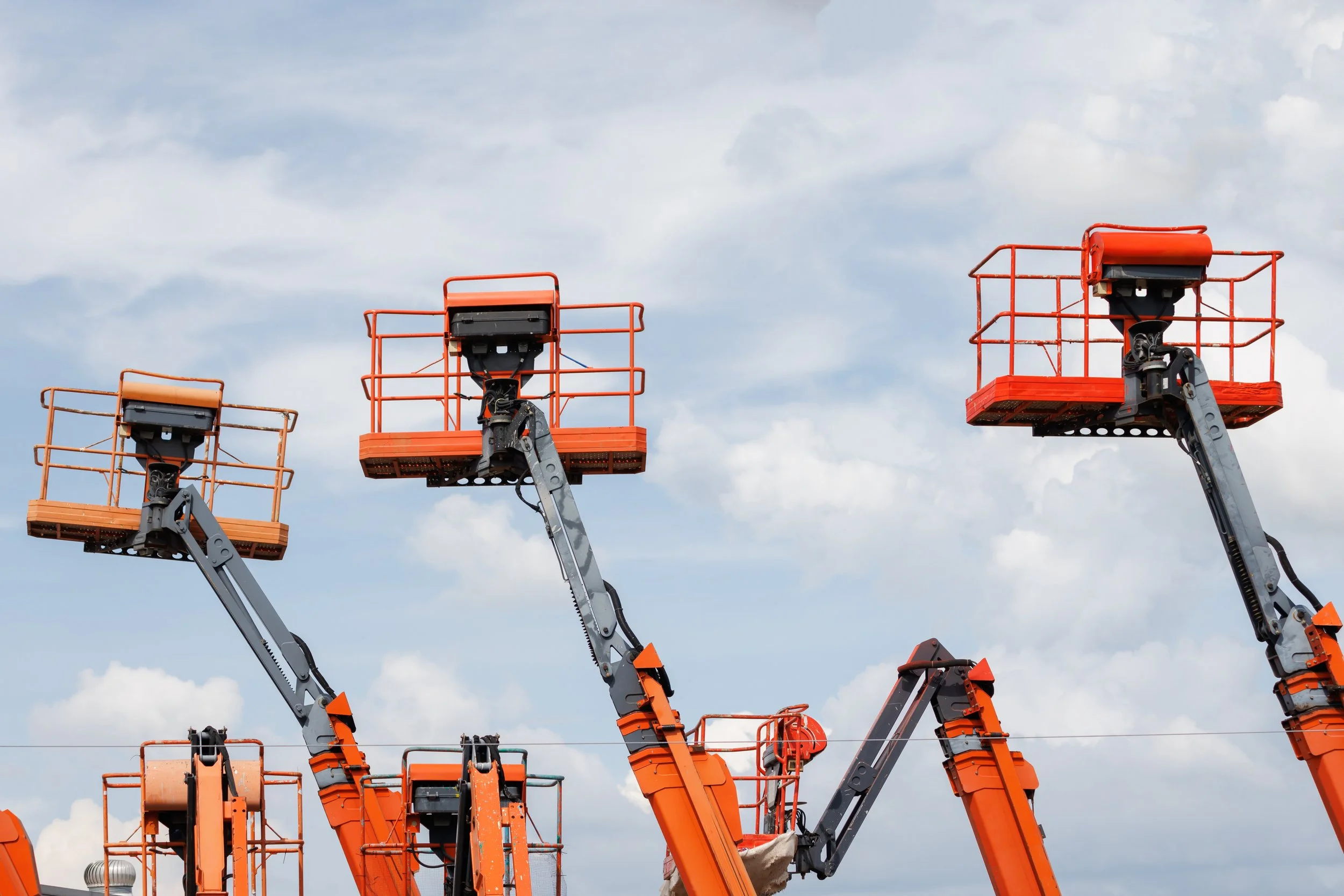 Multiple orange construction lift platforms are raised against a cloudy sky.