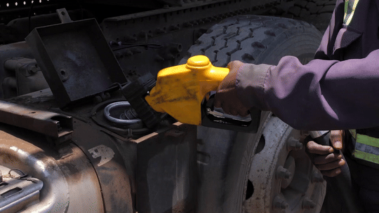 A person using a handheld device to inspect or diagnose a large vehicle or machinery, with a yellow cover on the device.