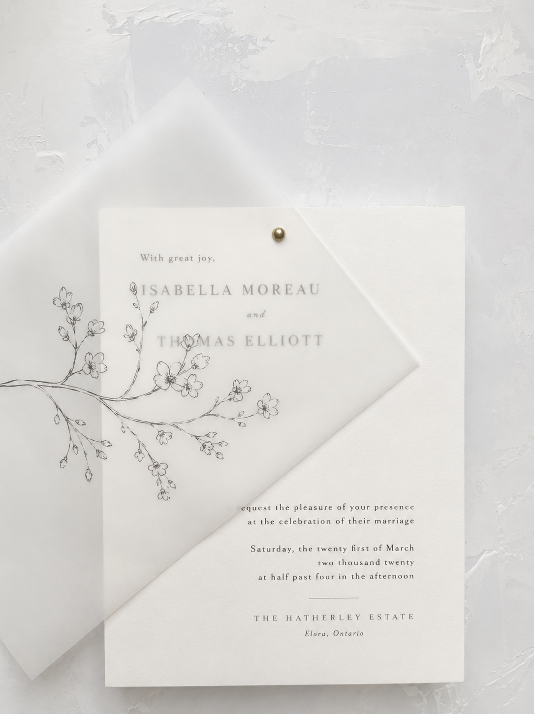Wedding invitation on white textured surface with transparent envelope and floral line art, announcing the marriage of Isabella Moreau and Thomas Elliott at The Hatherley Estate, Ontario.