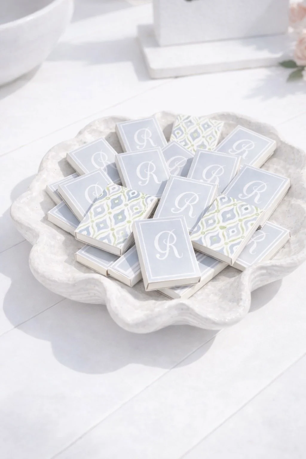 A white serving dish holding multiple small boxes with light blue covers bearing a white letter 'R' and a decorative pattern.