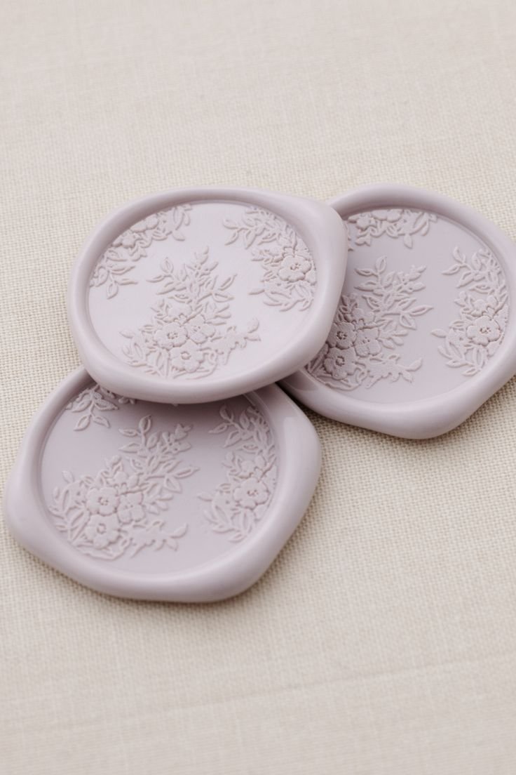 Three white soap bars with engraved floral patterns on a light-colored surface.