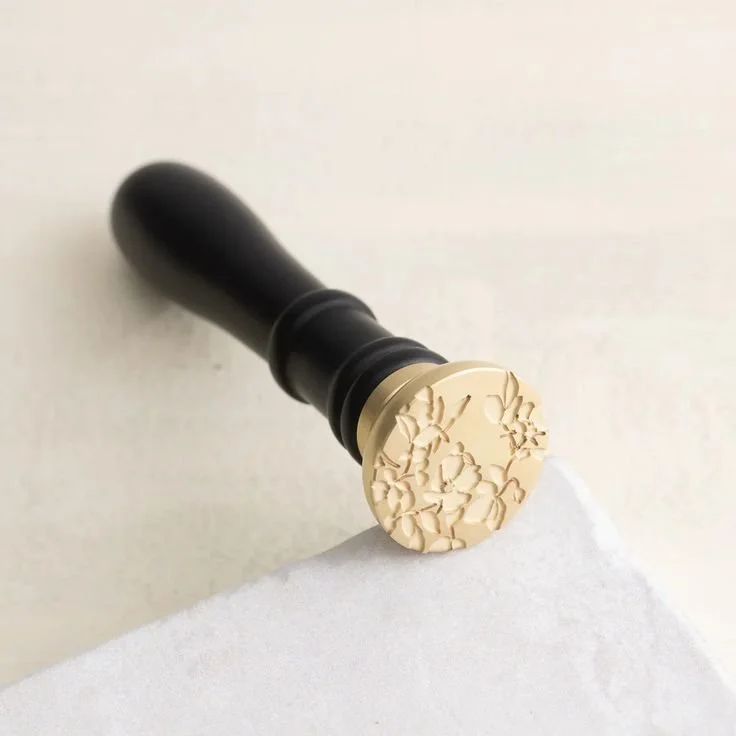 A rubber stamp with a black handle and a beige, intricately carved floral design on the stamp pad, resting on a white surface.
