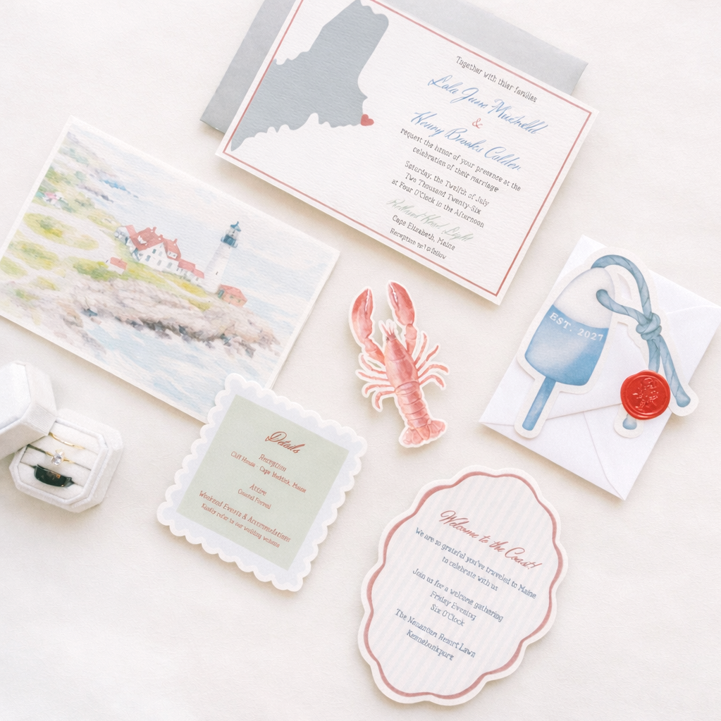 Wedding invitations and decorations including a map of Maine, a lighthouse illustration, a lobster sticker, a thank you note, an envelope with a blue tag and red wax seal, and a ring box.