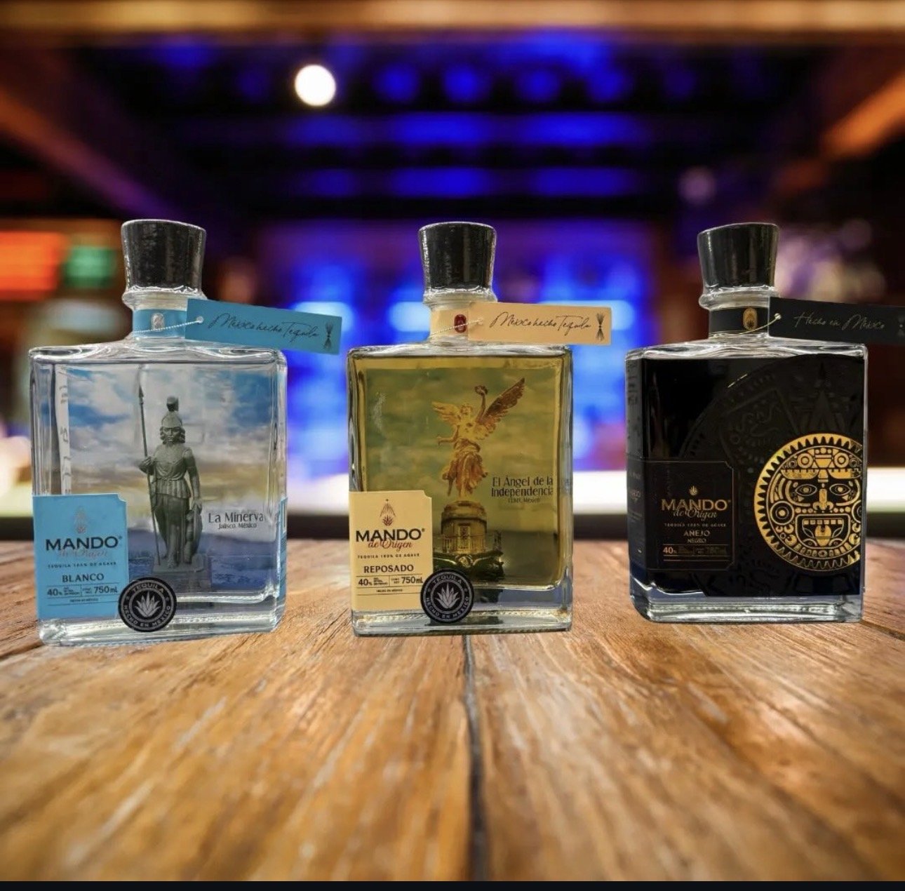 Three bottles of tequila on a wooden surface with a blurred bar or nightclub background.