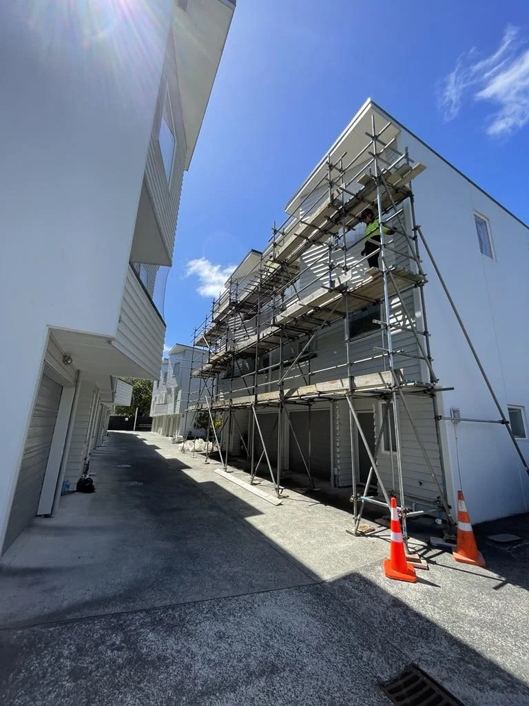 Construction worker on scaffolding working on a white multi-story building under a blue sky