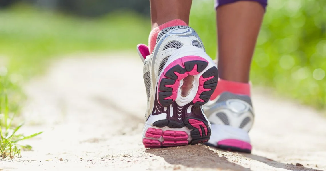 Person walking on a dirt trail wearing athletic shoes with pink and gray accents.