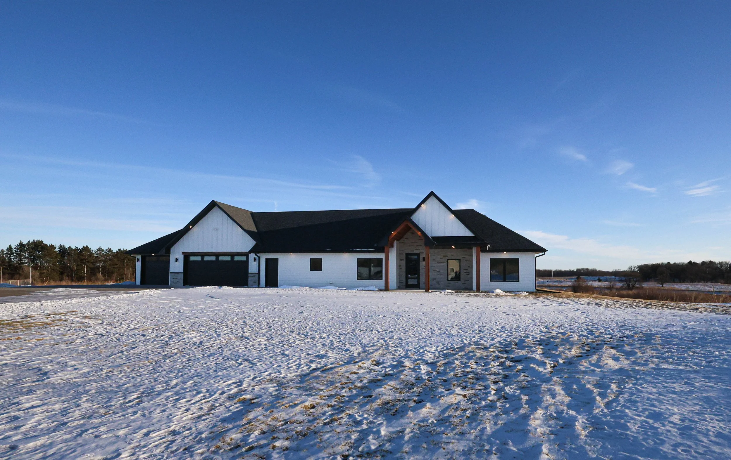 A modern house with a black roof and white walls, set in a snowy landscape under a clear blue sky.