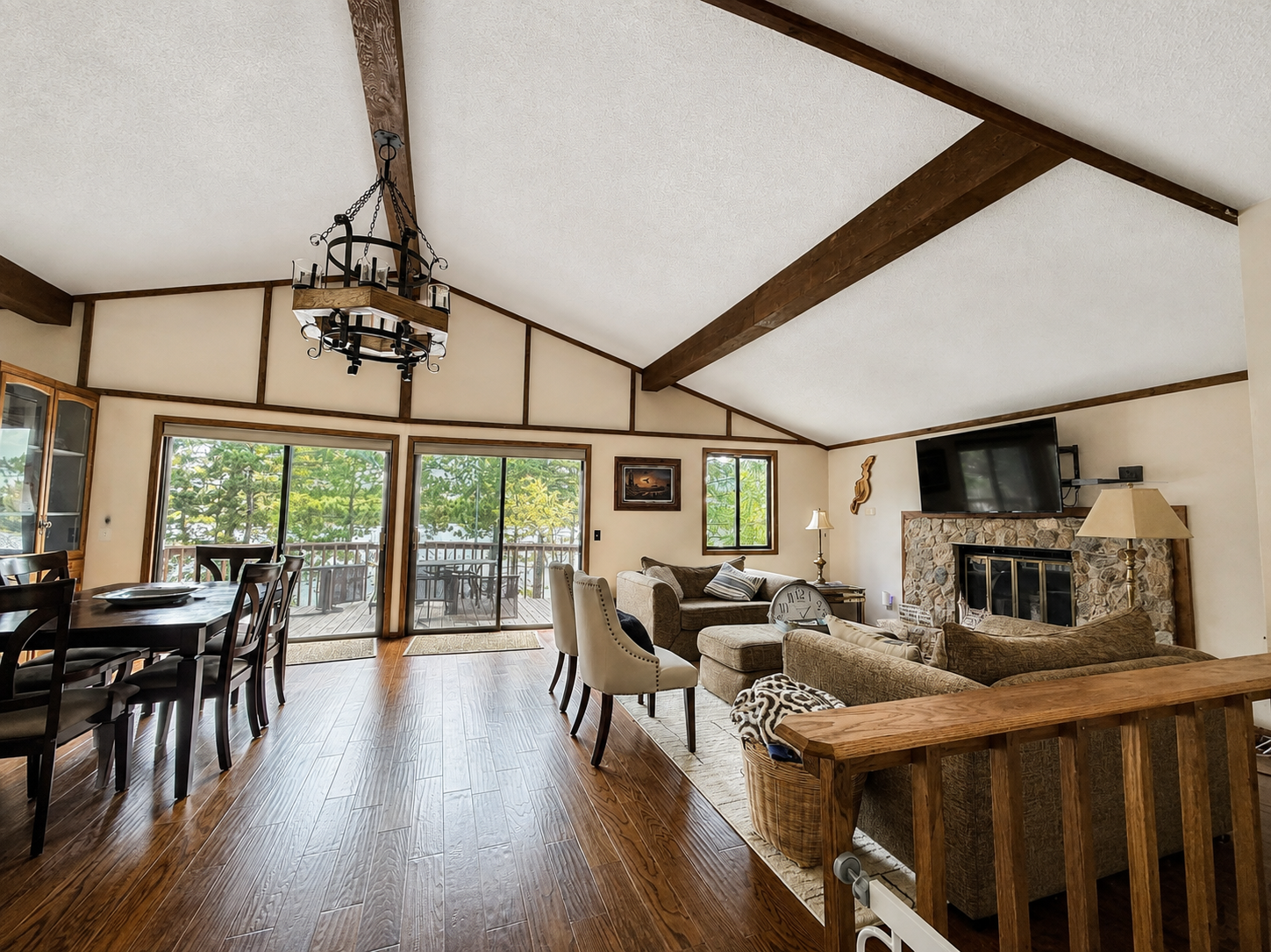 Living room with sliding glass doors leading to a deck, featuring wooden flooring, a stone fireplace with a large TV, and a sofa and chairs arranged for seating.