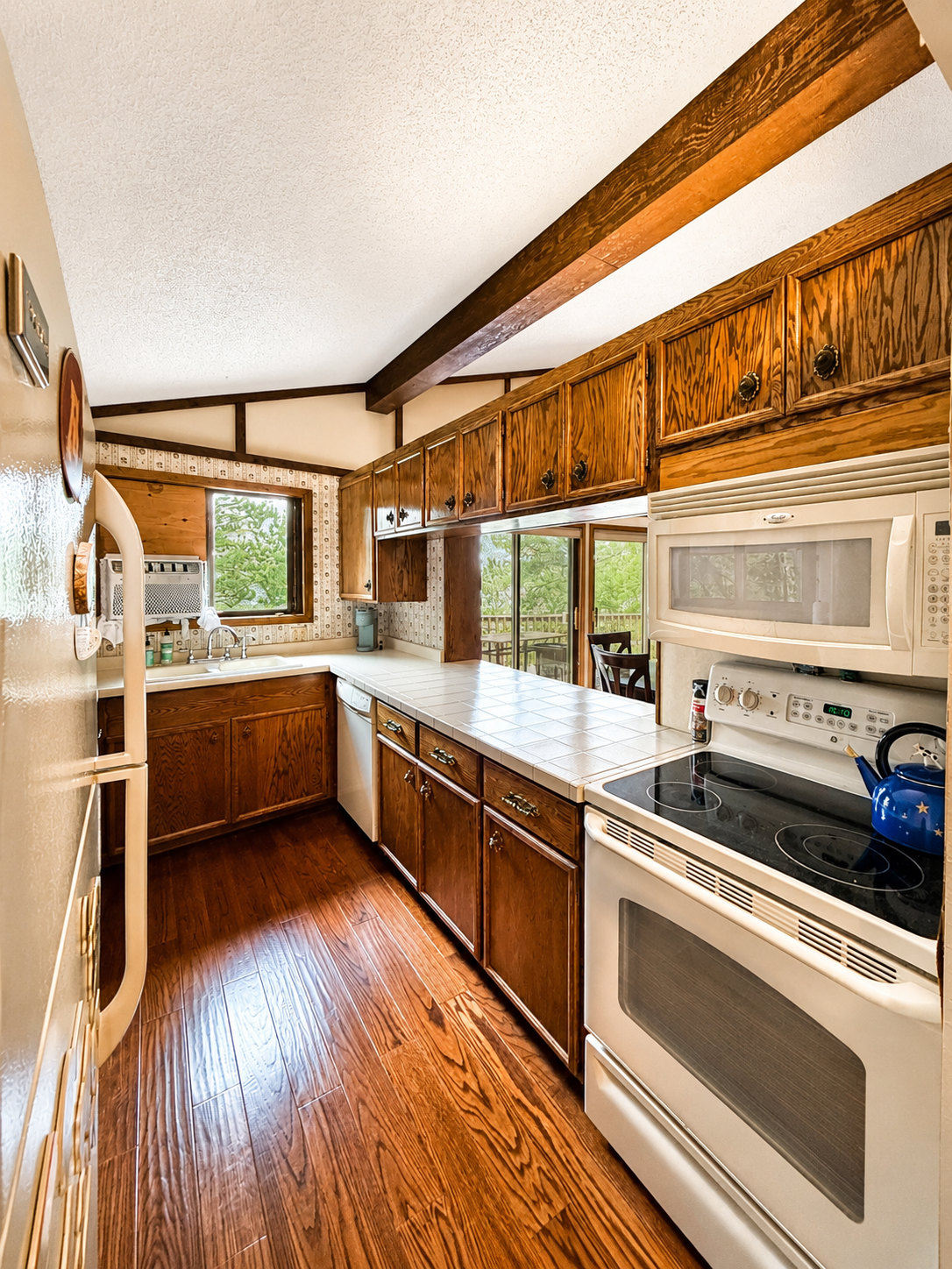 Kitchen with wood cabinets, white appliances, and a window over the sink overlooking greenery.