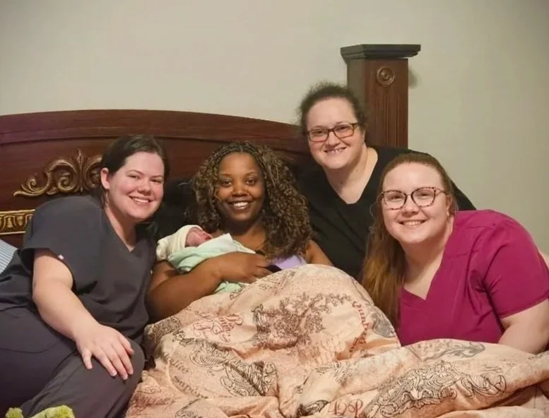Woman in bed holding newborn with clarksville midwifery team surrounding her
