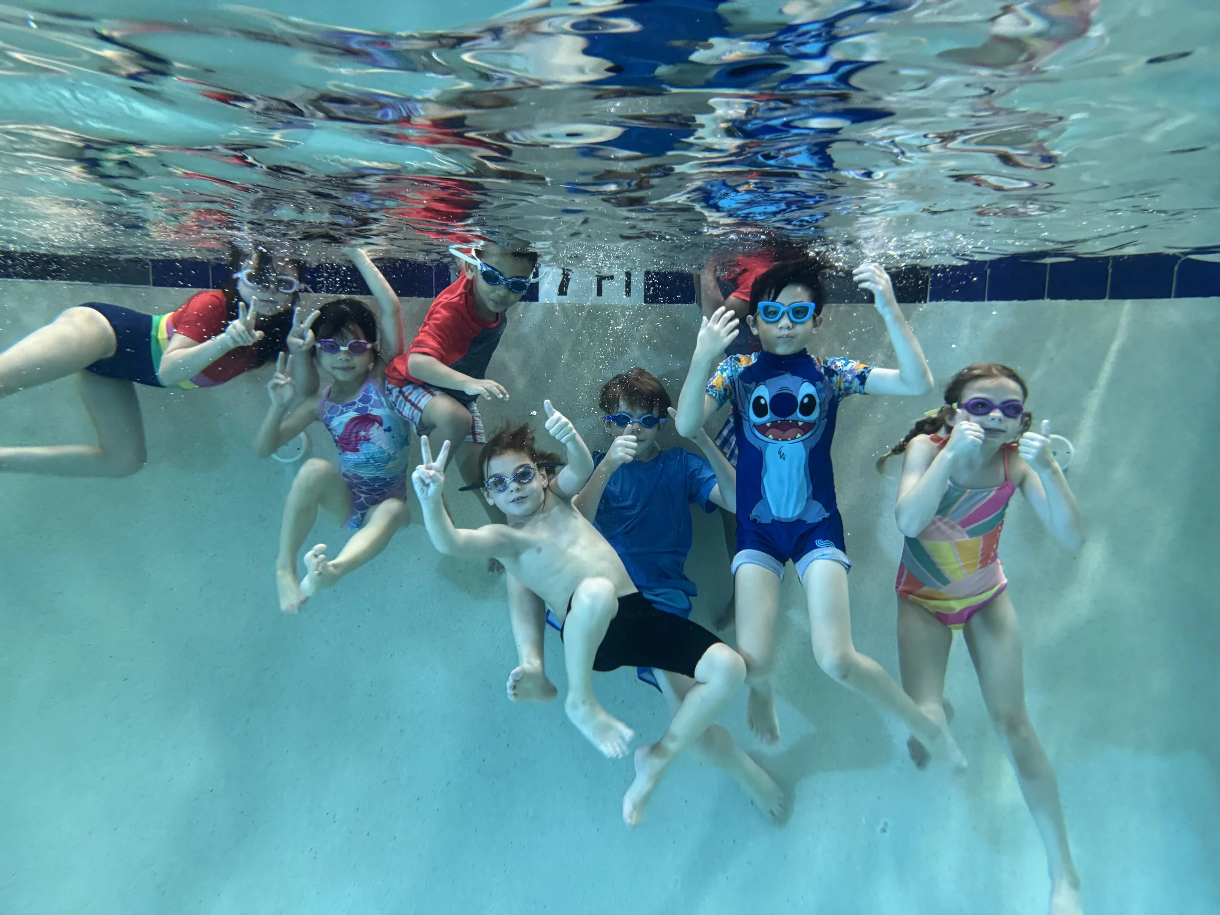 Group of children swimming underwater in the clean indoor pool at Sutton Swim School