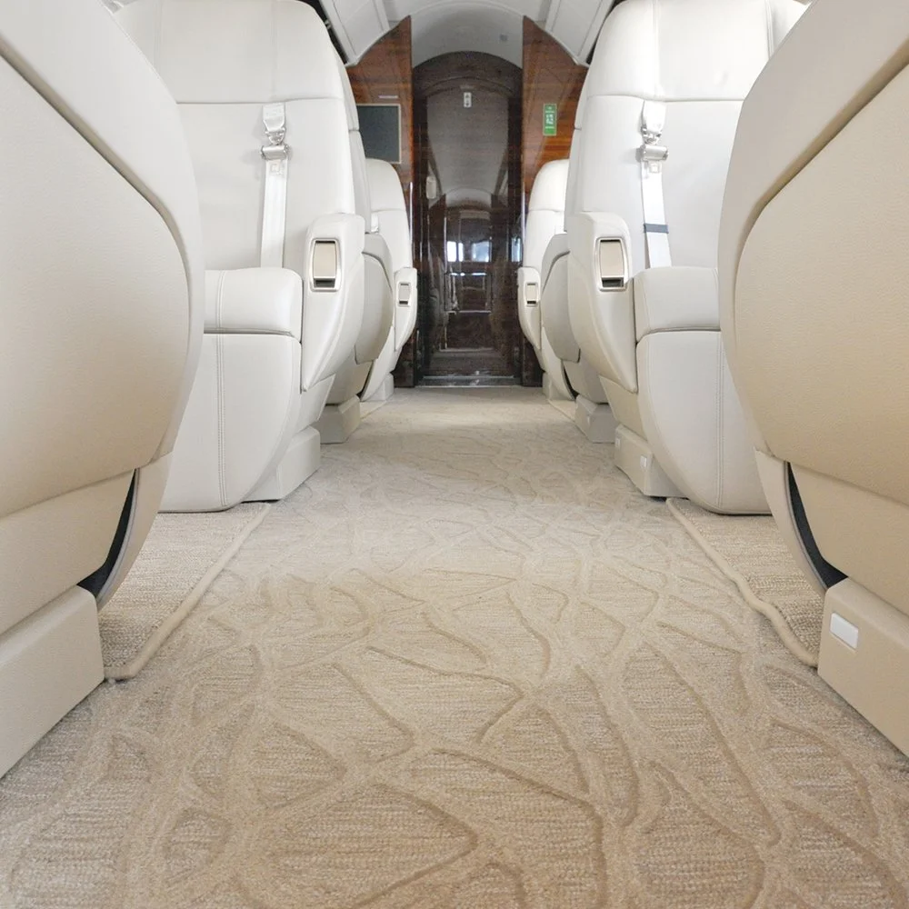 The interior of an aircraft cabin showing two rows of white leather seats with a central aisle and a door at the end.