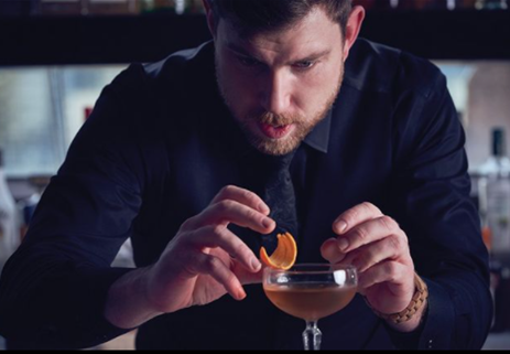 A bartender garnishing a cocktail with an orange peel.