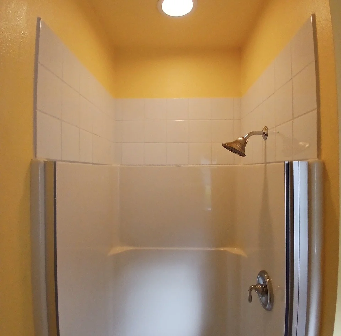 Shower with yellow ceiling, white tiled walls, metal showerhead, and divider.
