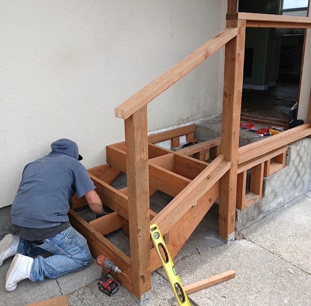 A person working on a wooden staircase frame outside a building.