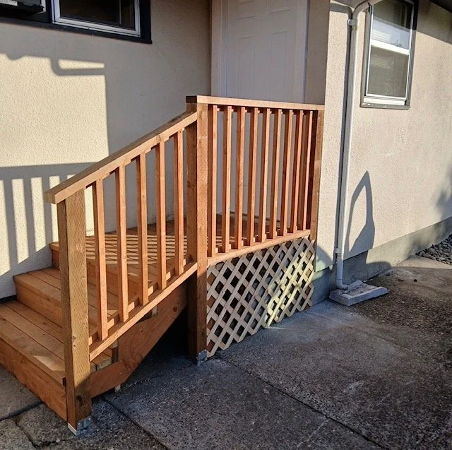 Wooden staircase and railing outside a house with a small lattice panel underneath.