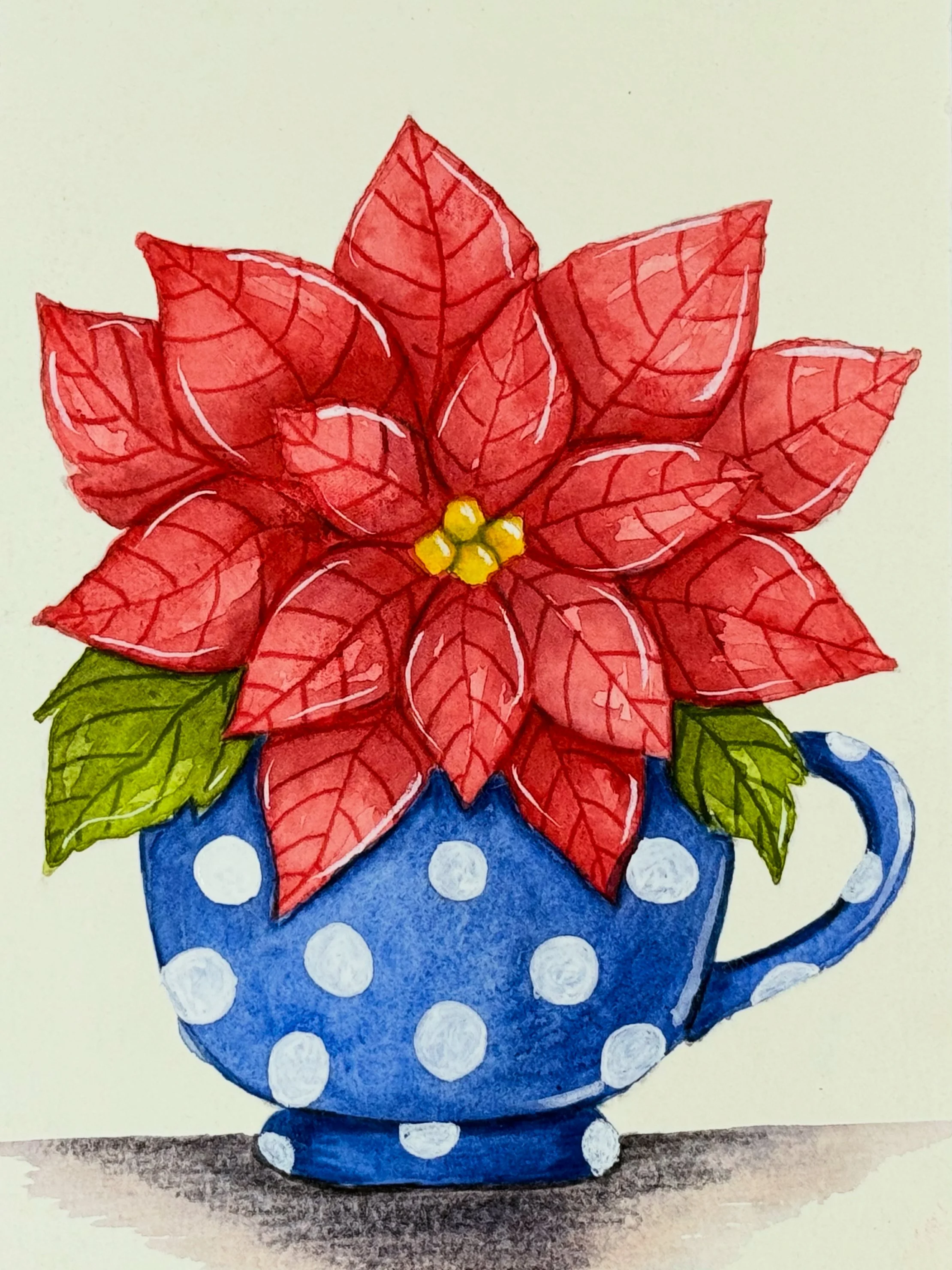 Watercolor painting of a poinsettia flower with red petals, green leaves, inside a blue polka-dotted mug.