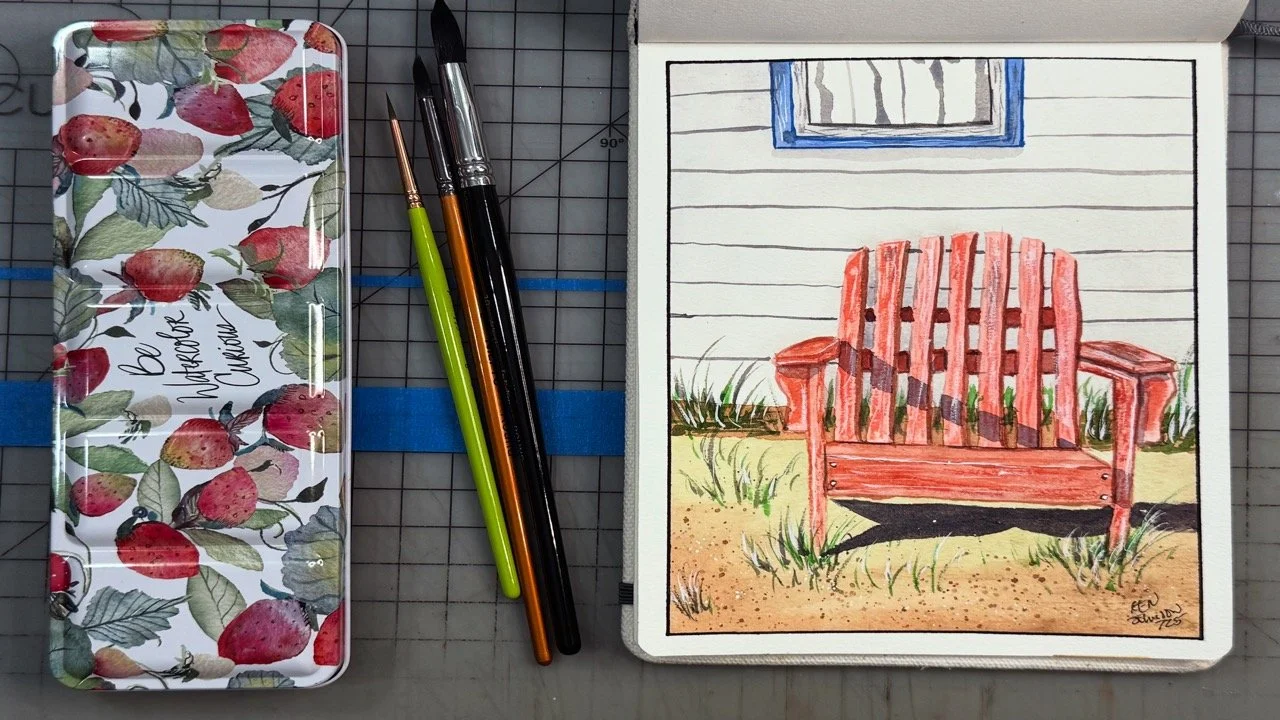 A watercolor painting of a red wooden bench on a grassy area in front of a house with white siding and a small window. The scene is displayed in an open sketchbook, with art supplies and a floral-patterned pencil case or tray nearby.
