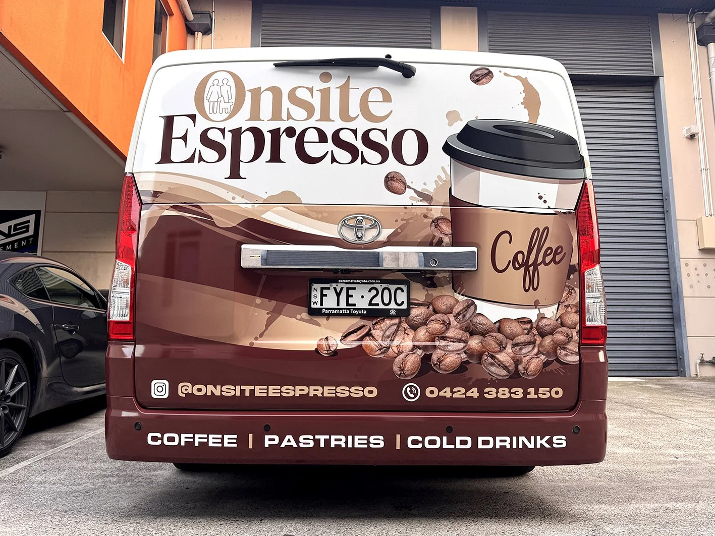 Rear of a delivery van decorated with coffee-themed graphics and text promoting coffee, pastries, and cold drinks. The van has a license plate reading FYE 20C and contact information, including social media handle and phone number.