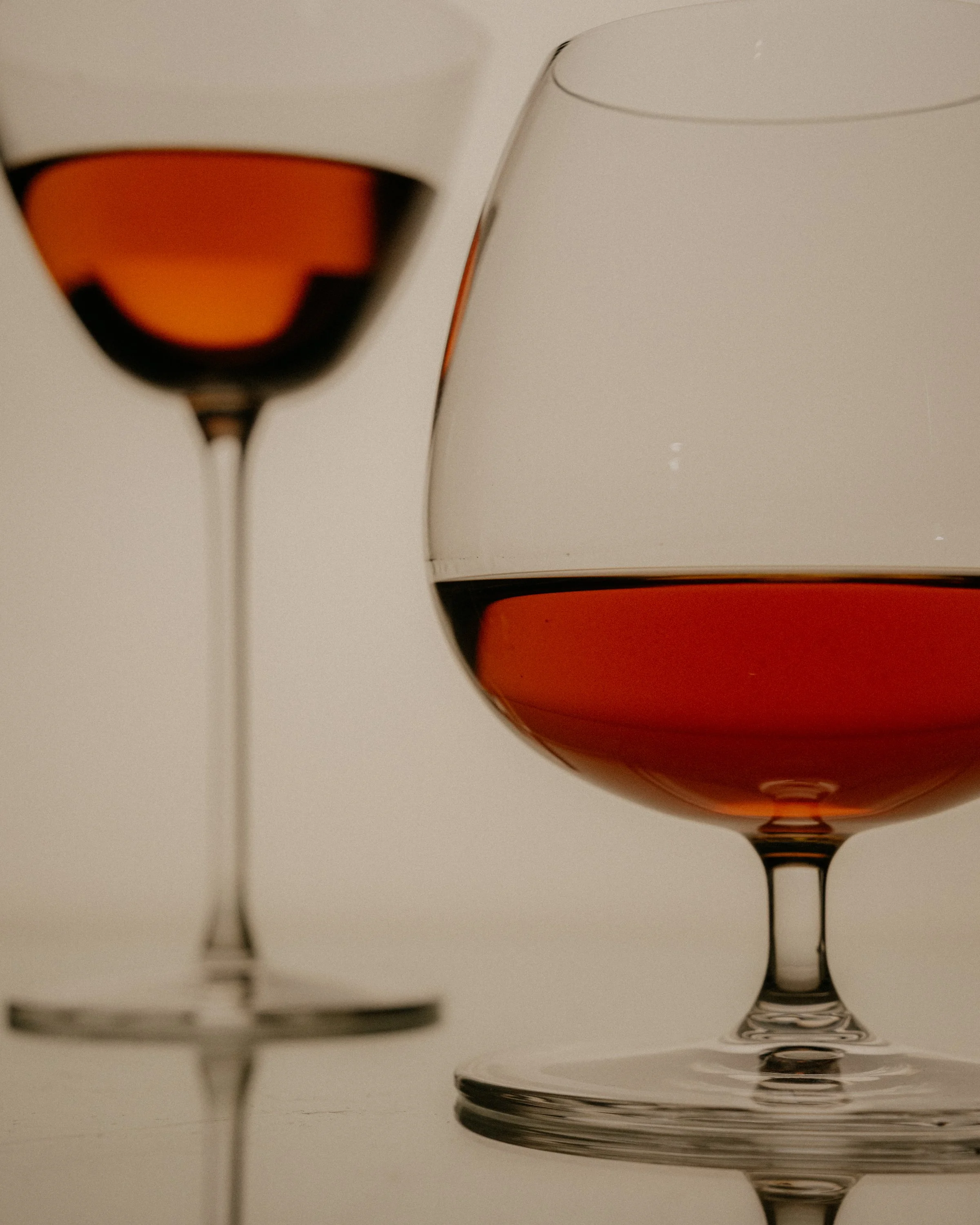 Close-up of two glasses of red wine on a white surface, with reflections and shadows.