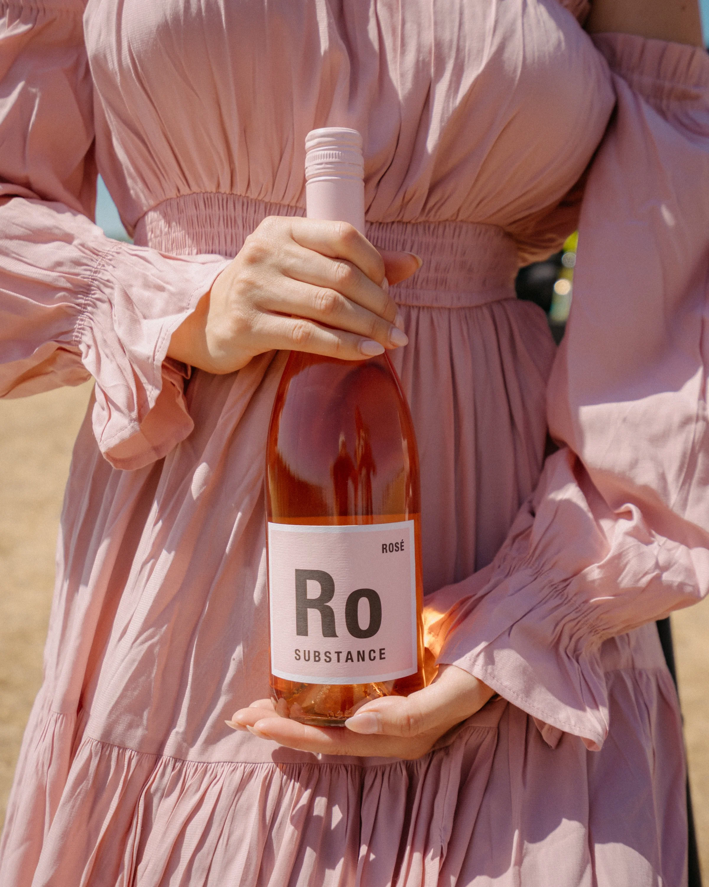 Person in a pink dress holding a bottle of rosé wine.