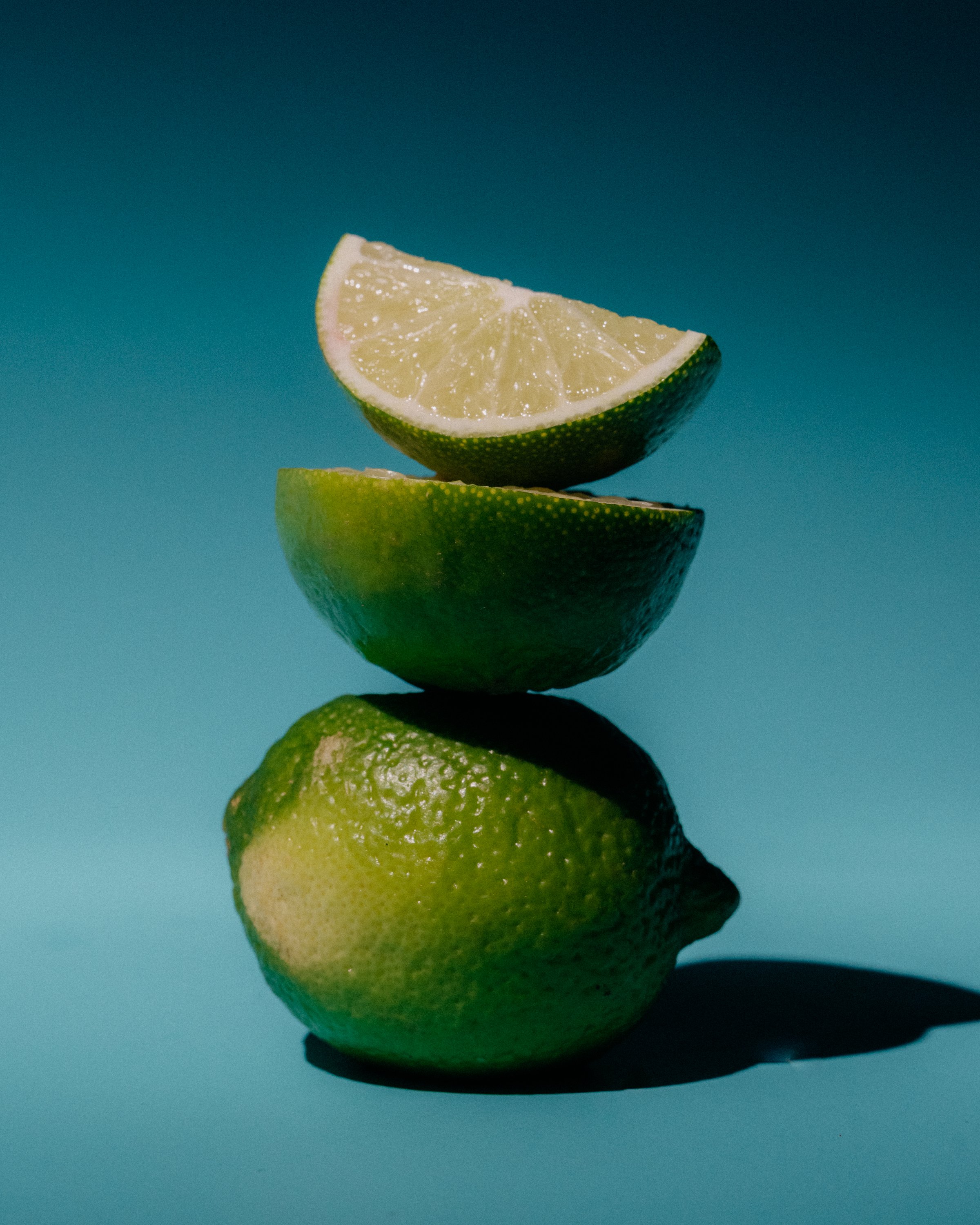 A lime cut into four pieces stacked on top of each other against a teal background.