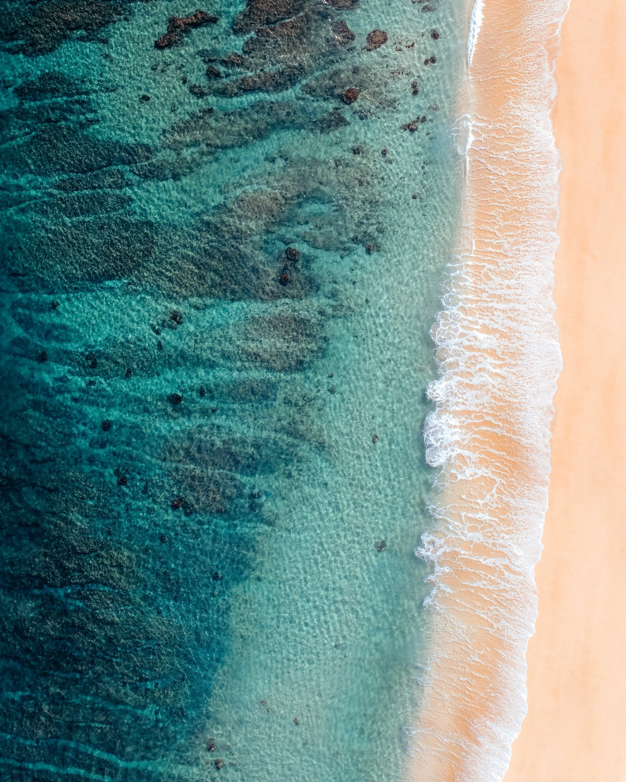 An aerial view of the ocean meeting a sandy beach with waves washing onto the shore.