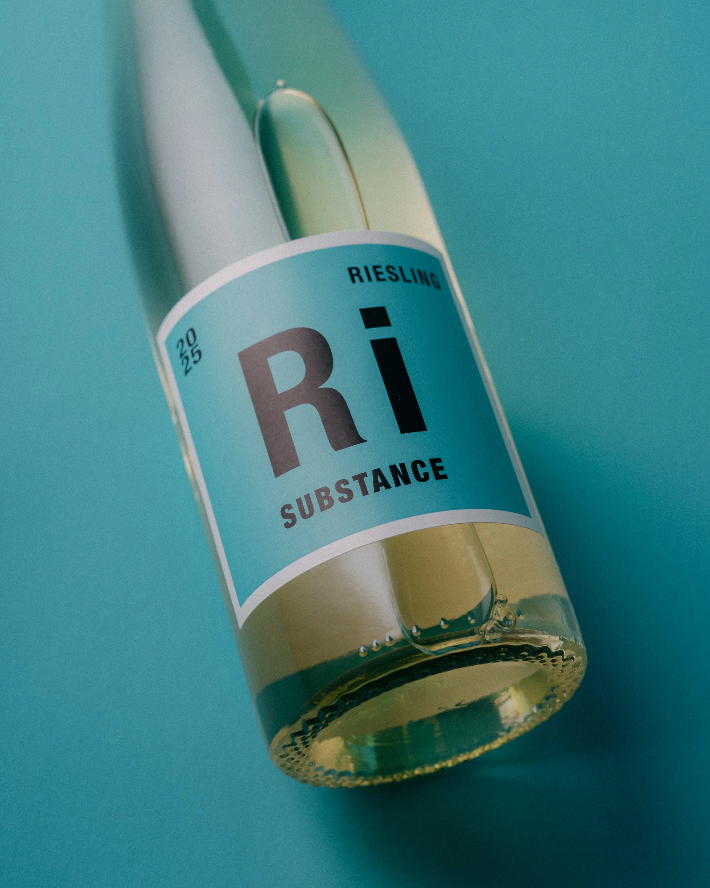 Close-up of a bottle with a light blue label reading "RIESLING" and "SUBSTANCE," against a teal background.