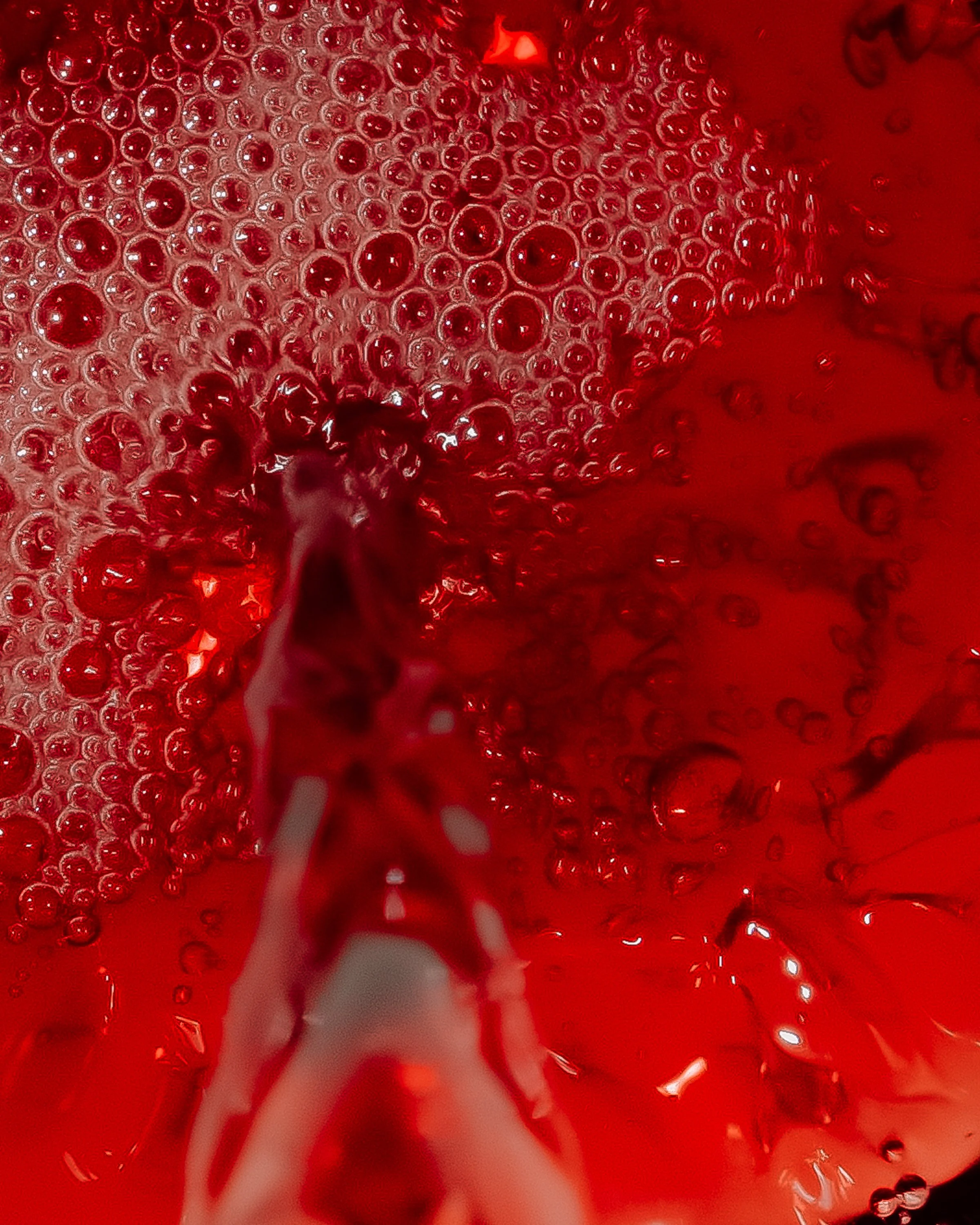Close-up of red liquid with bubbles and a pouring stream in water.